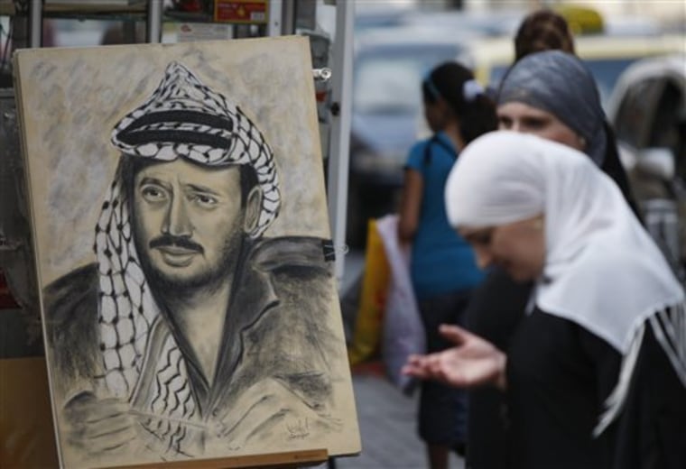 A Palestinian woman stands by a drawing of late Palestinian leader Yasser Arafat, displayed on a street corner in the West Bank city of Ramallah on Thursday. Palestinian President Mahmoud Abbas has said he's willing to exhume the body after doctors said they found elevated levels of the radioactive agent polonium-210 on clothing reportedly worn by Arafat before his death in November 2004. 